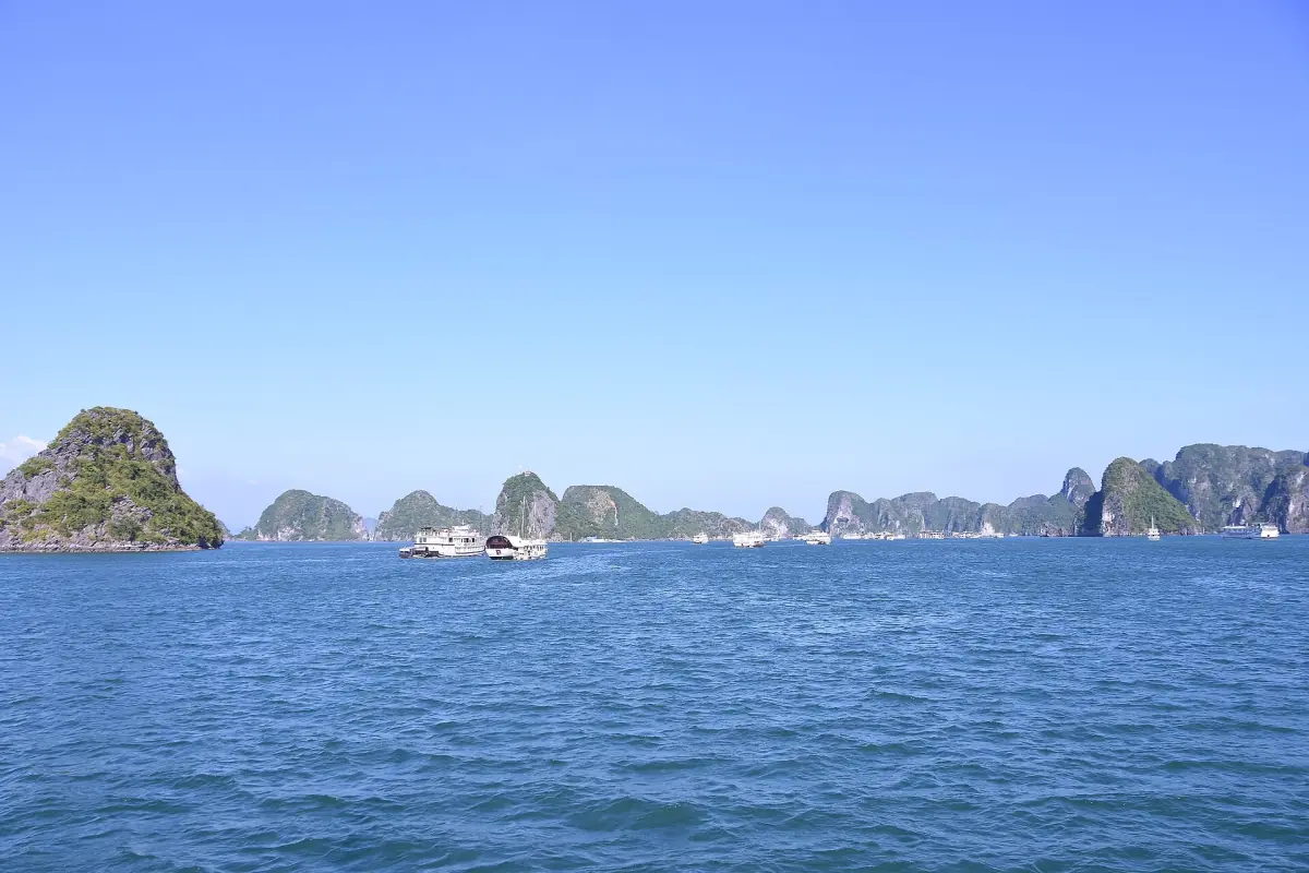 Kalksteininseln und Ausflugsboote in der Halong-Bucht unter klarem Himmel